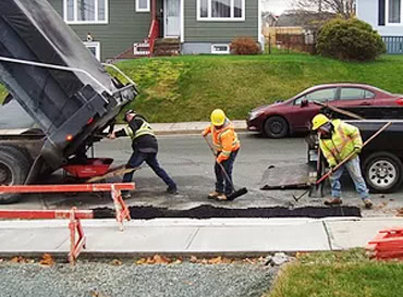 Road repair workers fixing asphalt on a city street with heavy machinery and tools.