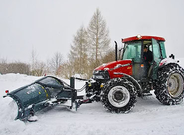 Tractor with snow plow clearing snow in winter conditions.