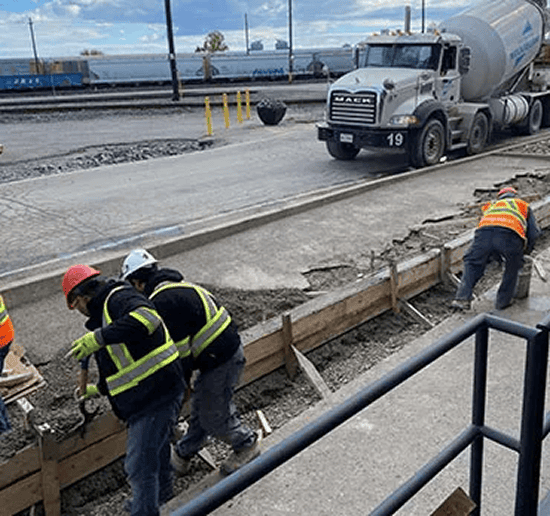 Construction workers pouring concrete on a sidewalk project.