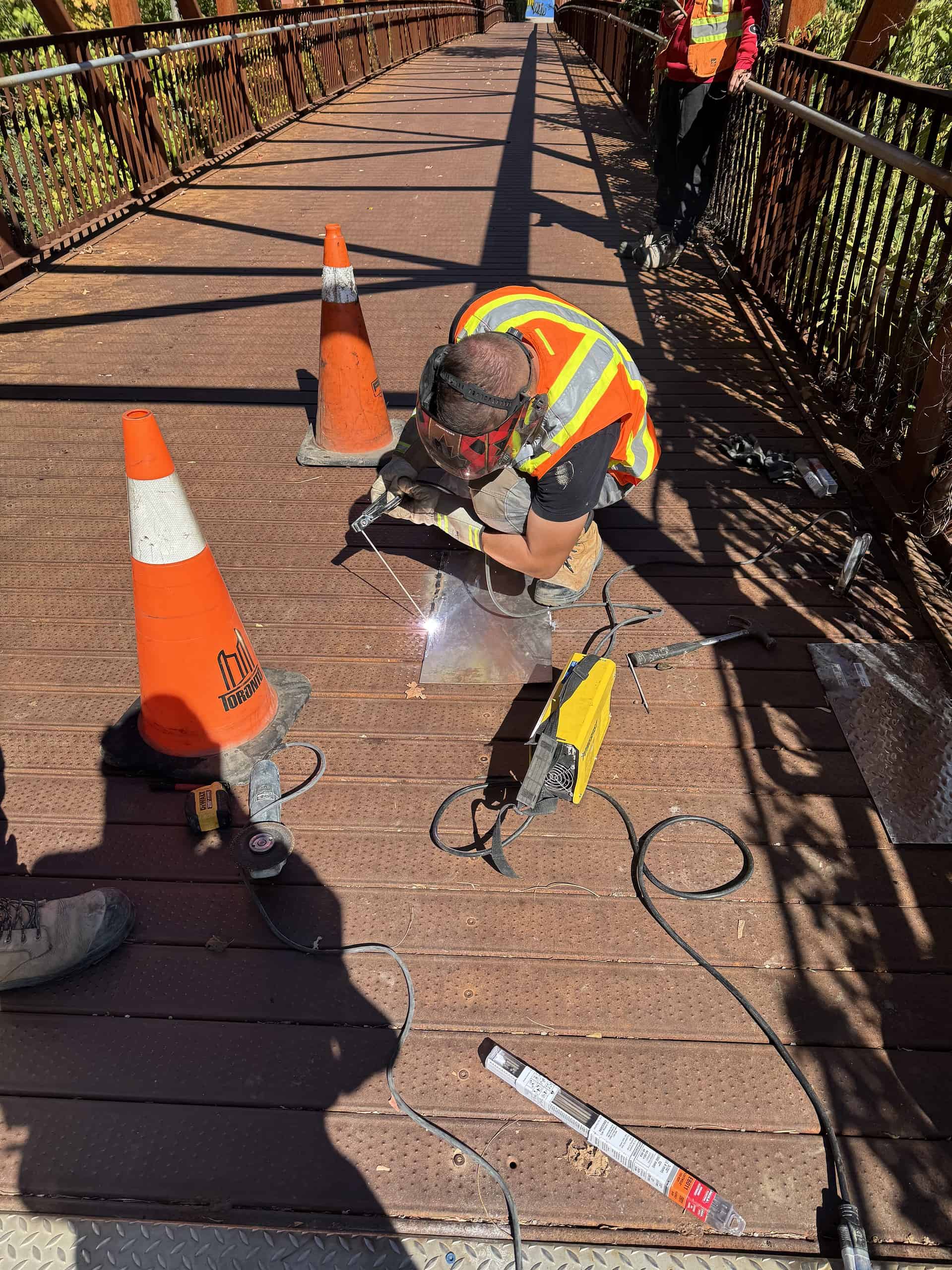 Welding on a metal bridge with safety cones and equipment, showcasing professional construction serv.