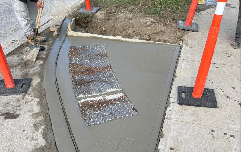 Concrete curb being poured and shaped at a construction site.
